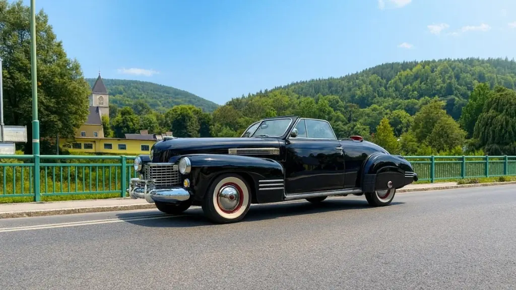 Schwarzes Cadillac Cabriolet mit Weißwandreifen auf einer Brücke vor Dorfkirche und bewaldeten Hügeln