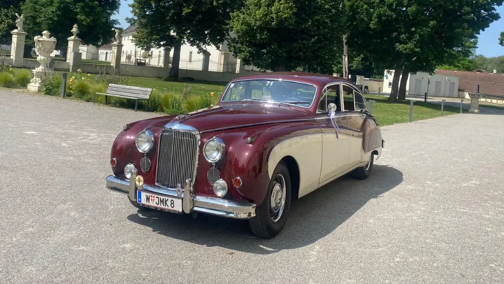 Zweifarbiger Jaguar Mark VIII in Bordeaux und Creme vor einem barocken Schlosspark im Sommer